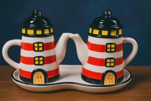 "Punavalko raidalliset, keraamiset, majakan näköiset pienet kannut tarjottimella öljyn, etikan tai salaatin kastikkeen tarjoiluun."